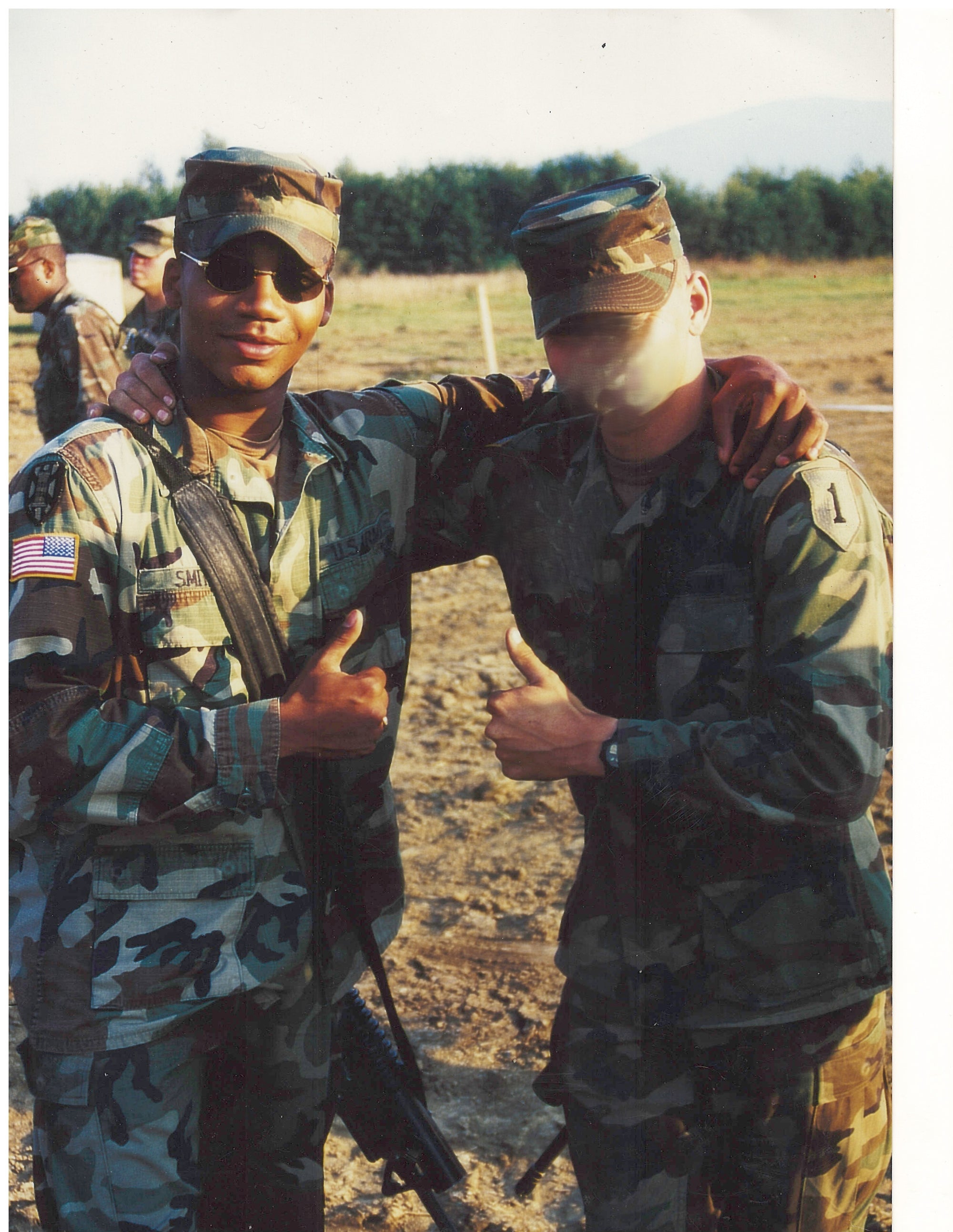 Two soldiers in camouflage uniforms standing outdoors on a deployment, with a clear sky.