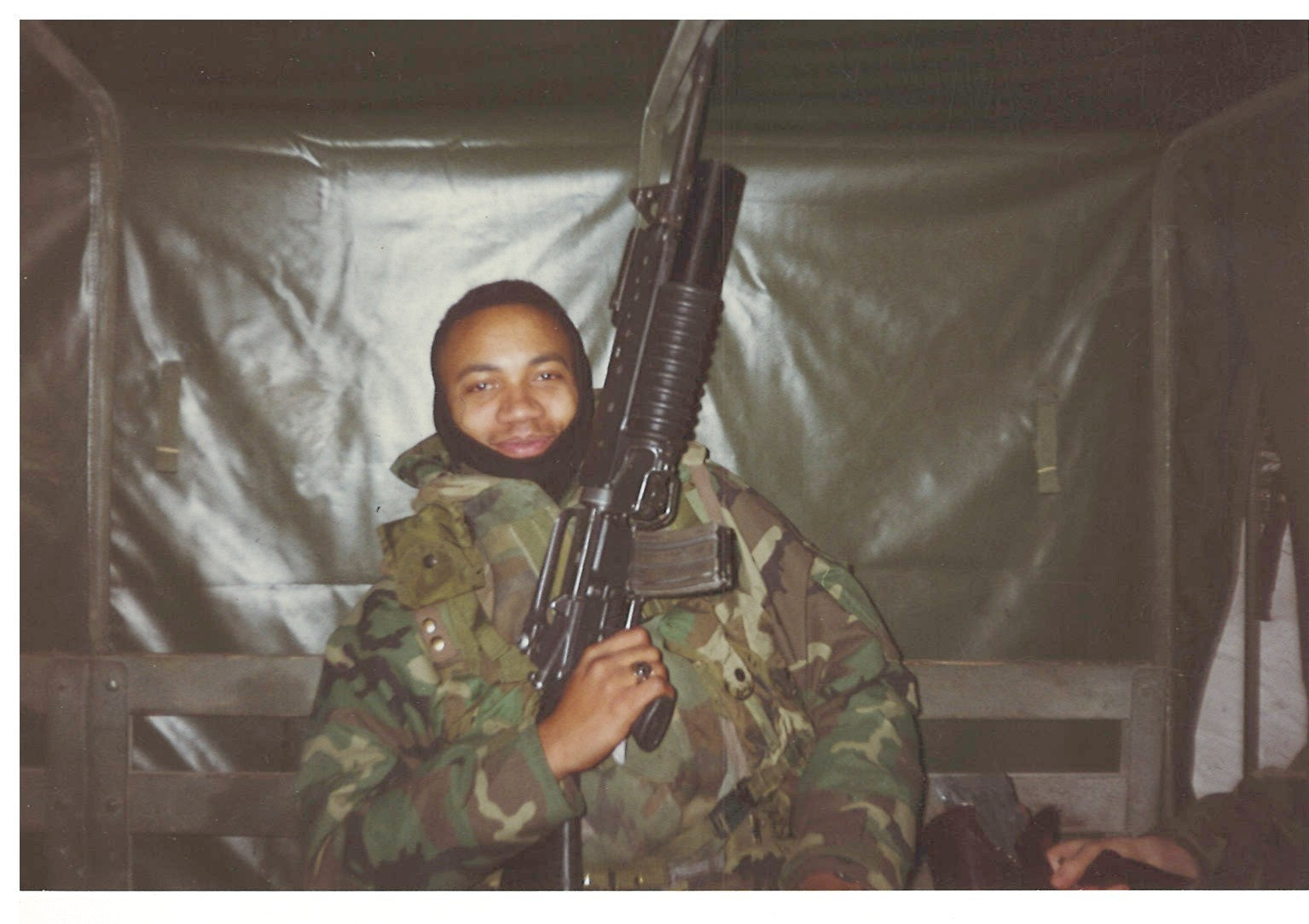 Person in military uniform holding a rifle inside a vehicle. The founder of Tactical Pause Apparel