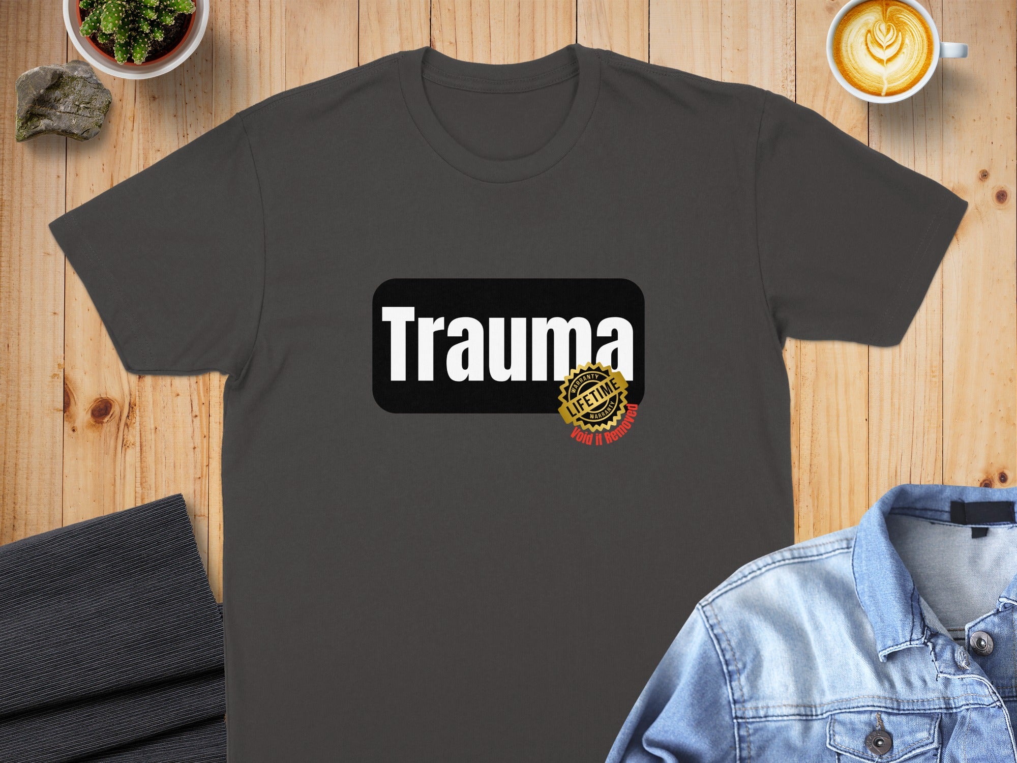 Dark t-shirt with "Trauma" in white text and a circular logo.